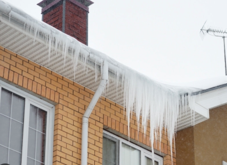 Close up of many icicles hanging off a roof in winter. The icicles have formed what's called an "ice dam" due to poor insulation in their attic.